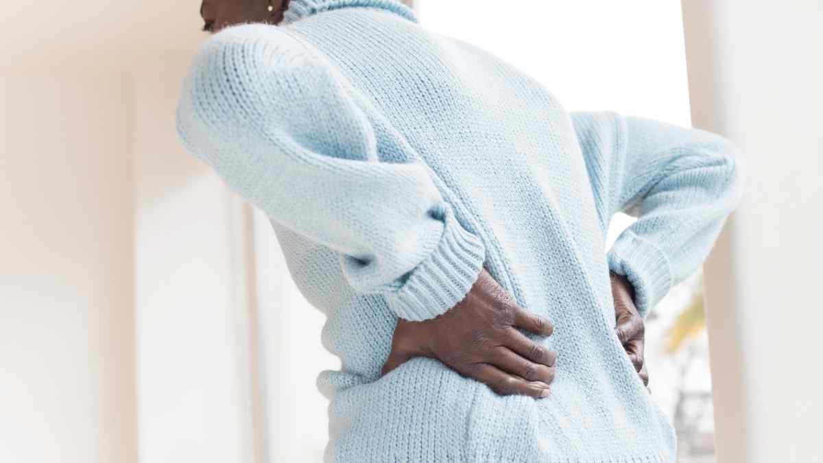 Pessoa de suéter claro com as duas mãos apoiadas na lombar